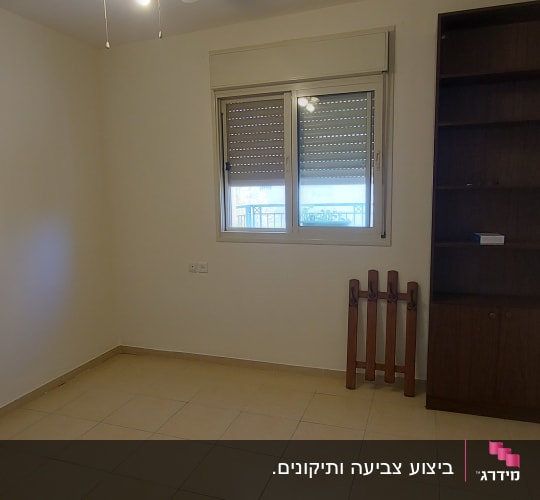 חדר מגורים צבוע בצבע בהיר עם כוננית ספרים וחלון